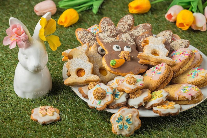 Different Easter cookies on a plate next to a porcelain hare with flowers in the grass