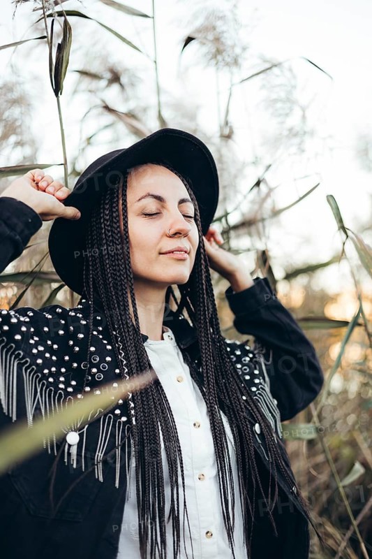 A serene woman enjoys a moment of tranquility at sunset, surrounded by natural greenery. Her peaceful expression reflects relaxation and harmony with the environment