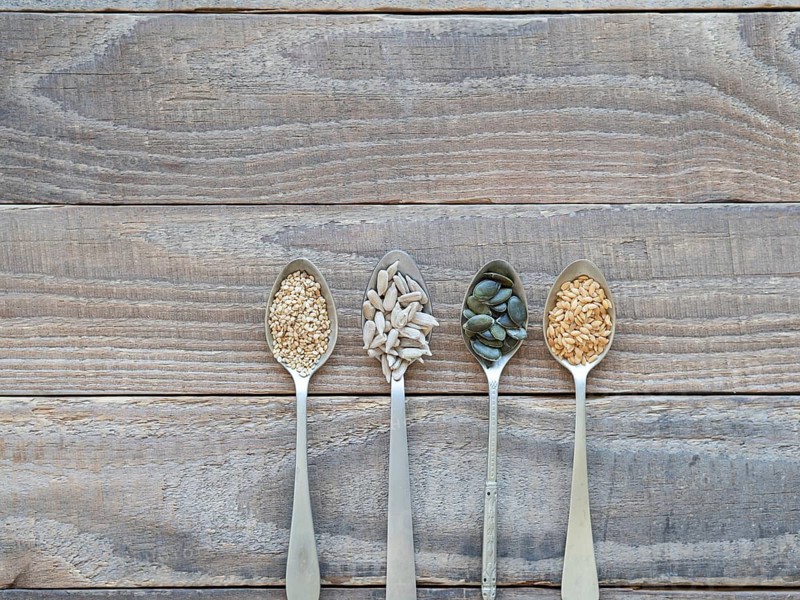 Various healthy seeds filling spoons on a rustic wooden table