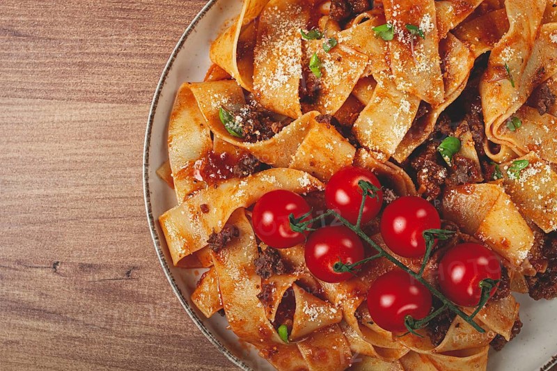 Pappardelle pasta with bolognese sauce, topped with parmesan cheese and cherry branch, homemade, no people