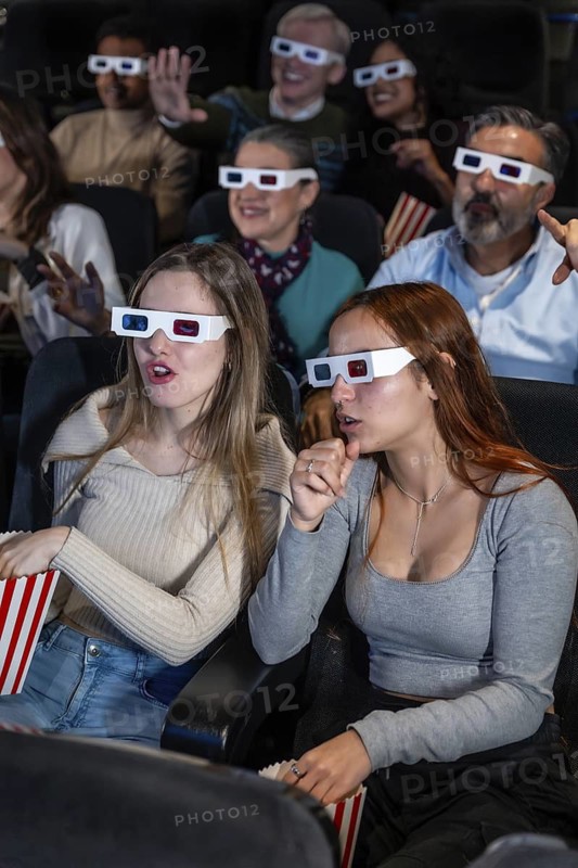 Group of diverse friends wearing 3d glasses enjoying a movie at the cinema, eating popcorn and experiencing reactions