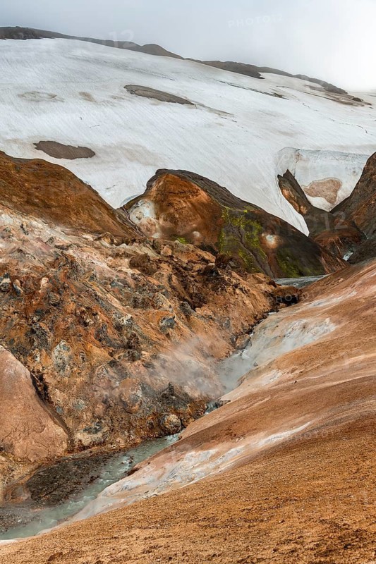 Steaming stream between colourful rhyolite mountains and snowfields, Hveradalir geothermal area, Kerlingarfjöll, Icelandic Highlands, Iceland
