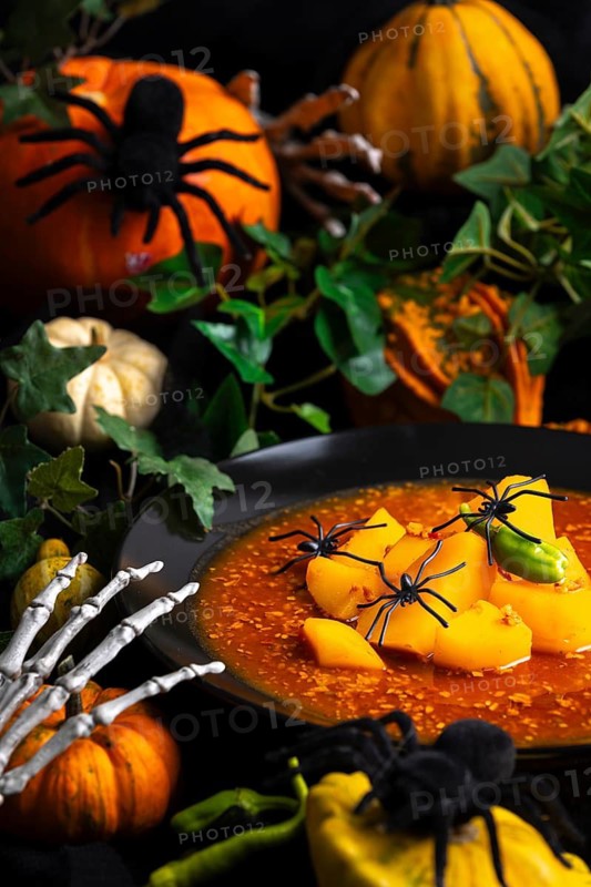 Halloween still life, goulash decorated with artificial spiders, pumpkins and green leaves, autumnal and dark, Halloween food