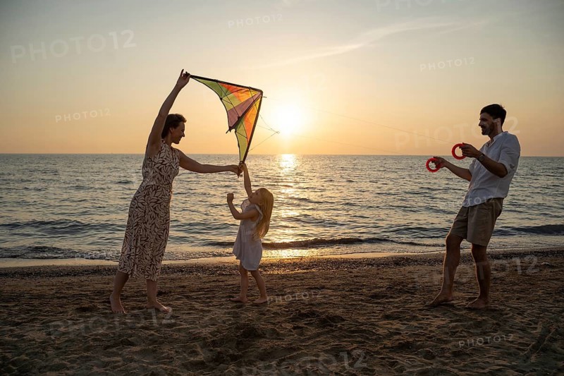 A family enjoys flying a kite on a picturesque Italian beach at sunset. The serene sea and warm golden light create a perfect backdrop for a joyful moment together