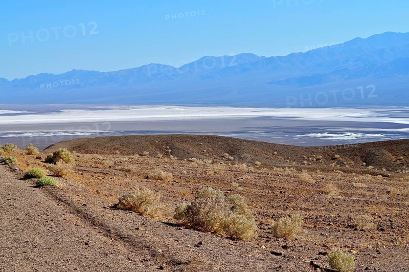 A barren landscape, with a salt pan in the foreground, surrounded by mountains under a blue sky, Artist Drive, Death Valley National Park, Mojave Desert, California, Nevada, USA