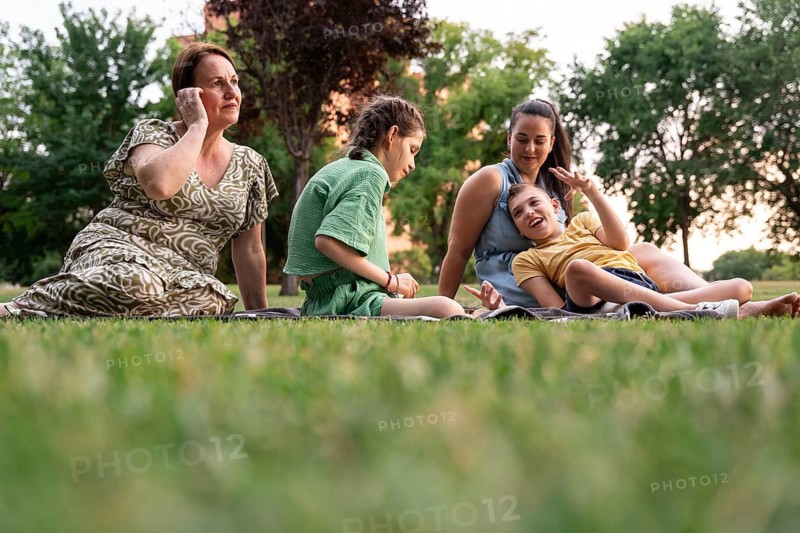 A loving family shares moments together in a grassy park. The image features a girl with a tracheostomy and a boy with cerebral palsy, highlighting joyful family interaction