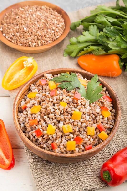 Buckwheat porridge with vegetables in wooden bowl on a white wooden background and linen textile. Side view, close up, selective focus. Russian traditional cuisine