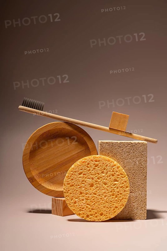 A bamboo toothbrush, eco-friendly toiletries, sponges, and soap are elegantly arranged on a neutral backdrop. The setup highlights sustainable living with natural materials
