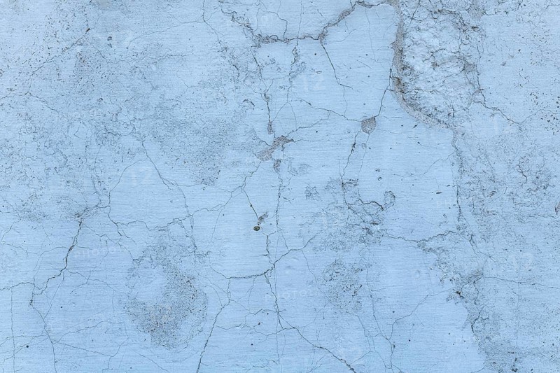 A close-up view of a weathered concrete surface displaying intricate cracks and texture, set in calming blue-gray tones. Ideal for backgrounds or design concepts