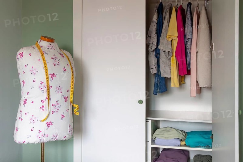 A well-organized closet with colorful clothes hanging neatly and folded on shelves, alongside a floral dress mannequin with measuring tape, conveys a sense of resale preparation