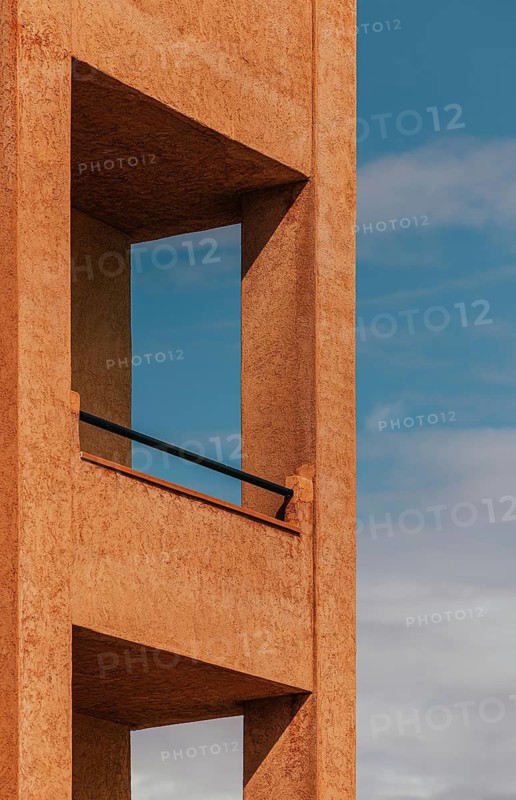 Minimalist architectural detail showcasing a modern structure with a textured facade against a vibrant blue sky. The design reflects simplicity and contemporary aesthetics