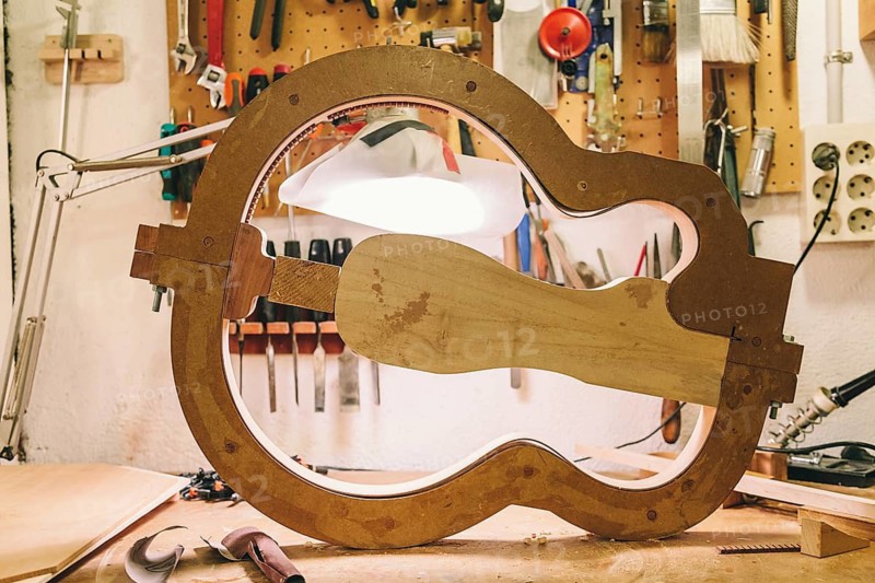 A detailed view of a bass guitar in progress at a luthier's workshop, showcasing tools and techniques used in crafting. The ambience captures the artistry involved in guitar making