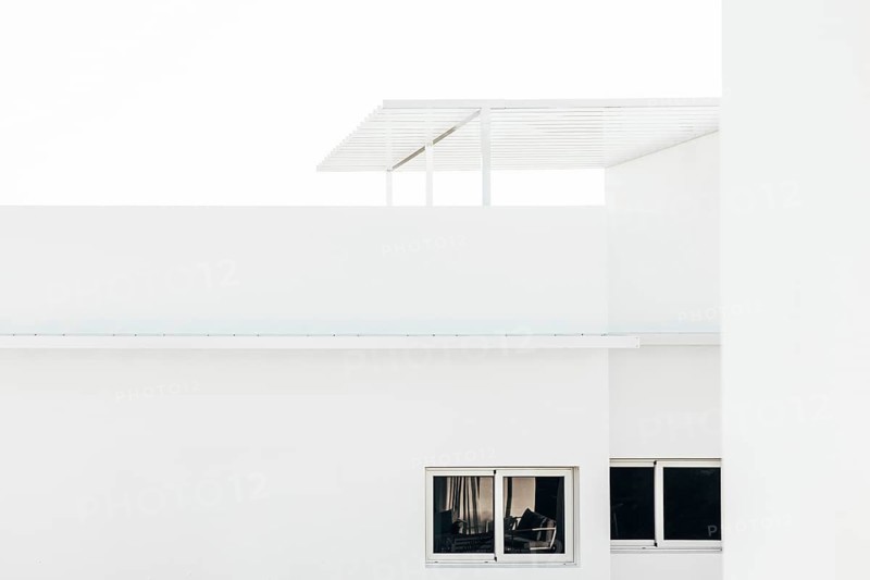 A modern minimalist architectural design featuring a white building with sharp clean lines, large windows, and a sleek pergola