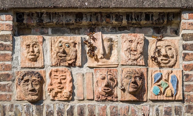 Artistic installation with mask and facial reliefs made of terracotta, in a historic brick wall, Warburg, North Rhine-Westphalia, Germany