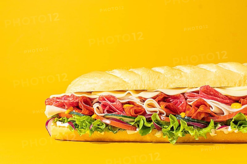 Close-up of a stacked deli sandwich, styled on a vibrant monochrome backdrop, with frontal lighting to emphasize depth and detail