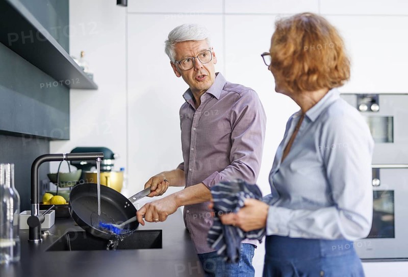 Symbolic photo. An elderly couple stand in the kitchen and do the washing up together. Berlin, 13.08.2024