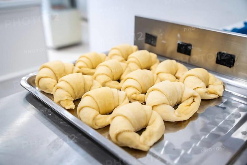 Croissant dough developing on a metal baking tray, prepared for baking in a commercial kitchen setting, showing the preparation stage of fresh pastries