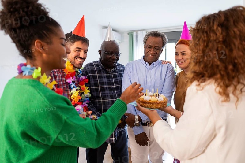 A lively group of people celebrating a birthday with colorful party hats and a cake. They share smiles, creating a warm and festive atmosphere full of happiness