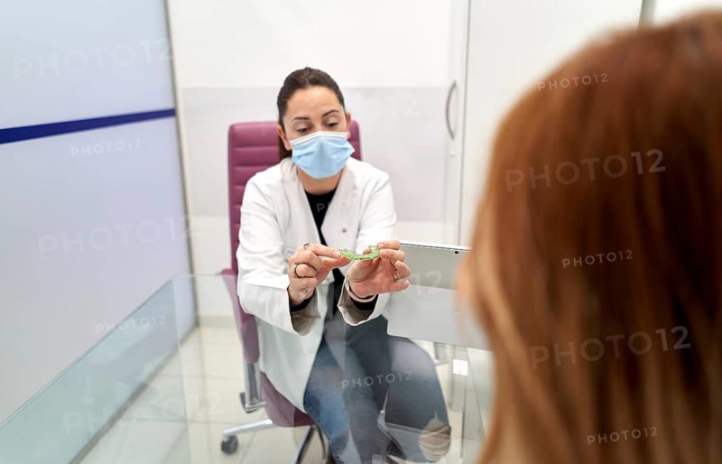A dentist wearing a mask educates a patient about dental care, displaying a teeth model in a modern clinic. The consultation emphasizes hygiene and patient education