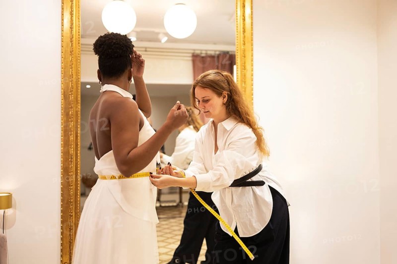 A tailor ensures a perfect fit by measuring a client waist in an elegant bridal fitting room. The scene reflects precision and attention to detail in dressmaking