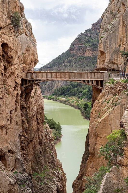A wooden bridge hovers over a river, surrounded by dramatic cliffs on the Caminito del Rey hiking trail, Malaga, Spain