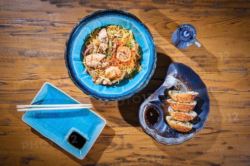 Wok noodles with shrimps and chicken, gyoza dumplings and soy sauce served on a wooden table, composing a delicious asian meal