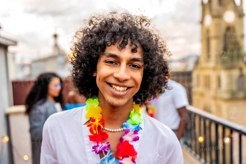Happy man with curly hair and Hawaiian necklace smiling during partying on rooftop