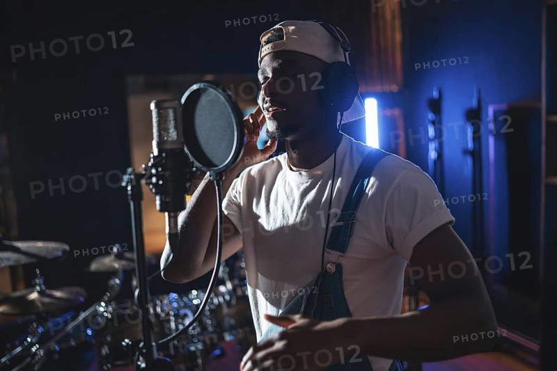 Young black artist wearing headphones and singing into microphone, recording a new album in professional music studio