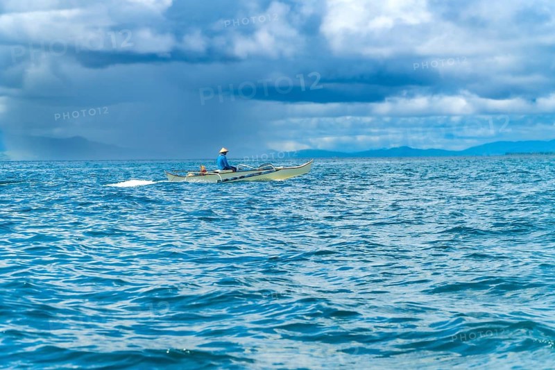 Traditional outrigger boat sailing on the tranquil blue sea surrounding siargao island, philippines, with a fisherman at the helm