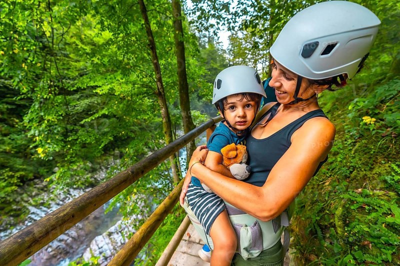 Mother carrying her son in a baby carrier while visiting the scenic vintgar gorge near bled, slovenia, during a summer day