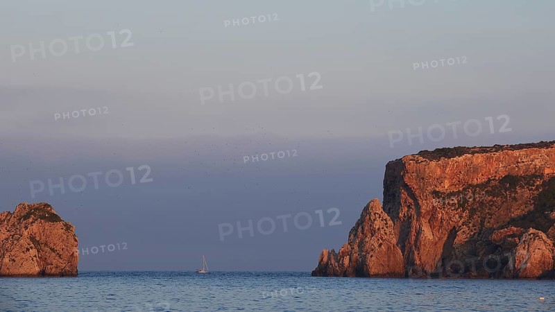 Cliff landscape with a sailboat off the coast at sunrise, morning light, islet of Tsichli Babas, island of Sfaktiria, Navarino Bay, Pylos, Peloponnese, Greece