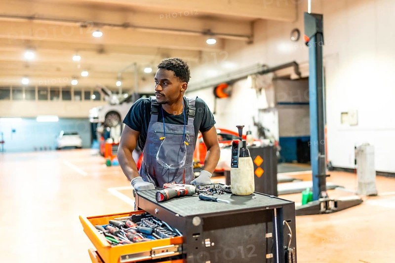 Young mechanic working on a car in a professional garage, using tools and equipment to perform maintenance and repairs
