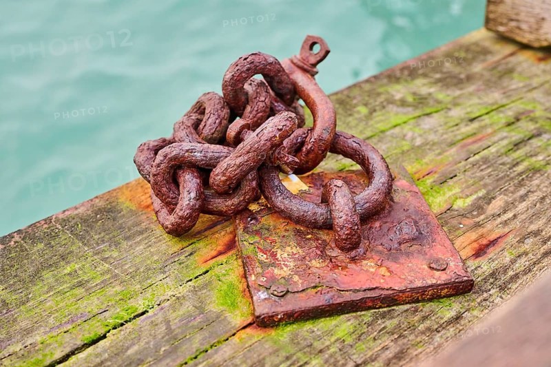 Old rusty chain on a wood at the harbor in Venice on a foggy morning in winter, Italy