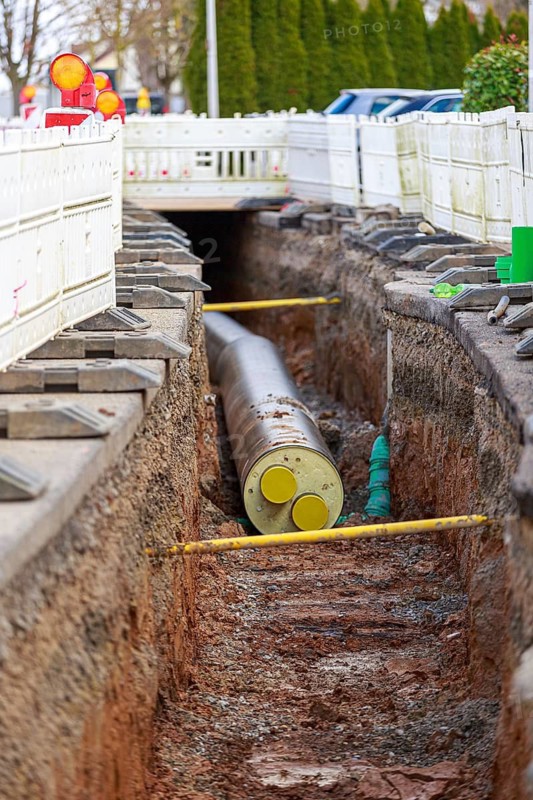 Open trench with a large district heating pipe and white barriers on a road