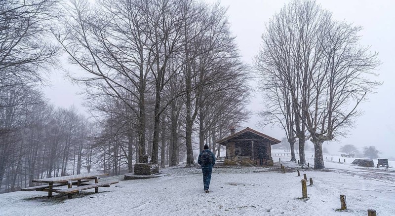 A young man walking next to the refuge of mount aizkorri in gipuzkoa. Snowy landscape by winter snows. Basque Country, Spain