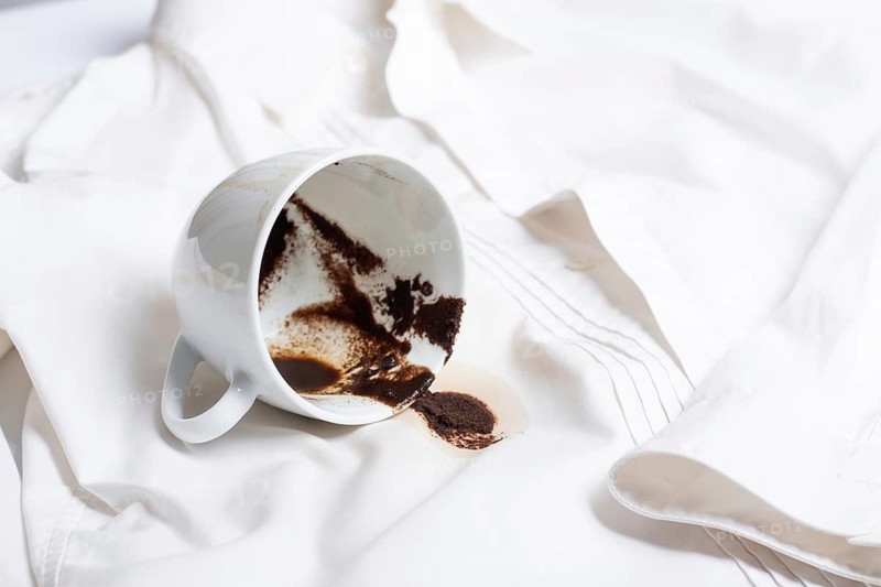 A white cup with the remains of coffee, spilled, lies on a white shirt, there are no people, a soft focus