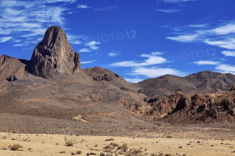 Picture of a dry desert landscape with a majestic, rocky mountain under a clear blue sky, The landscape of the Ahaggar Mountains in the Sahara in Algeria