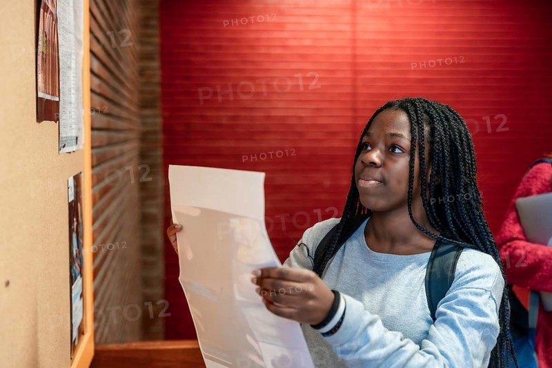 Young student consulting a bulletin board in a university hallway, focusing on important announcements and information for academic success