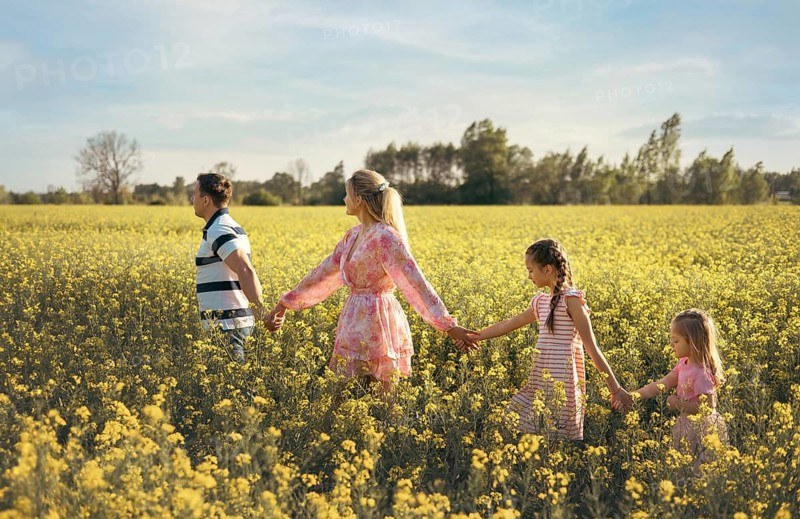 A joyful family walks together through a golden flower field, holding hands and enjoying the beauty of nature. The warm sunlight highlights their love, unity, and connection