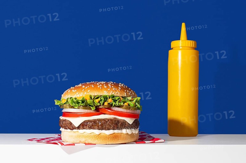 A vibrant image showcasing a delicious cheeseburger paired with a bright yellow mustard bottle, set against a stark blue background. The fresh ingredients and striking contrast make this a perfect choice for food-related themes