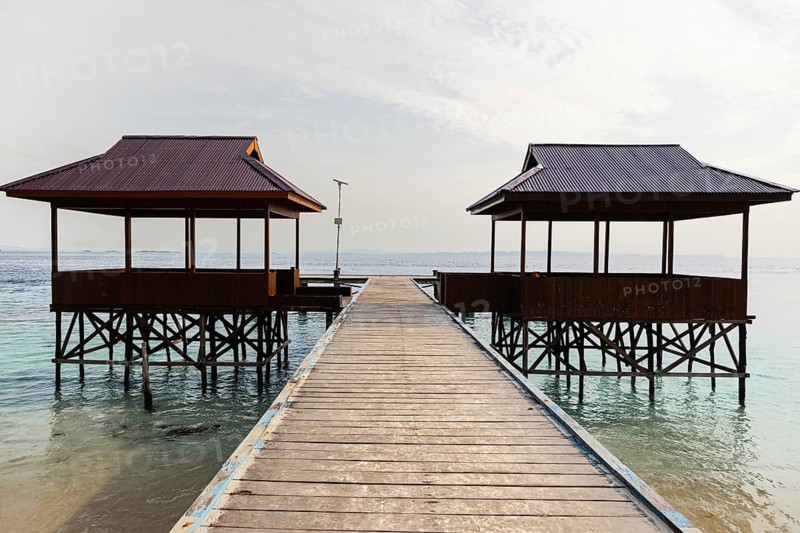 Top view of two traditional overwater gazebos connected by a wooden pathway in the pristine Raja Ampat archipelago, showcasing the clear turquoise waters and peaceful scenery