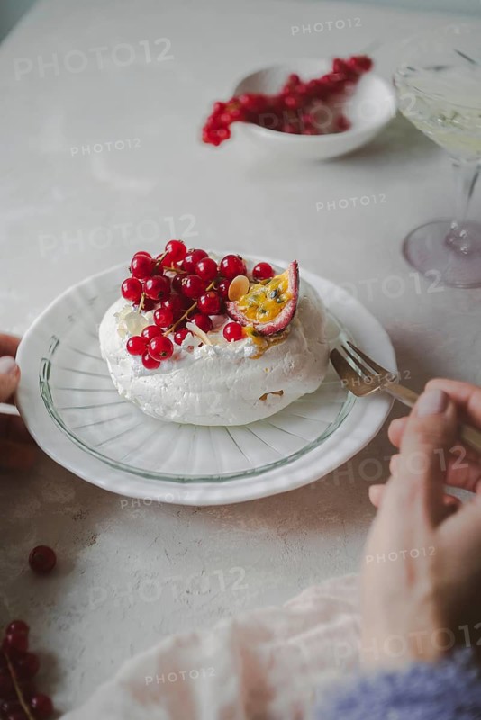 Cropped unrecognizable woman tasting a delectable red currant and passion fruit pavlova on a plate