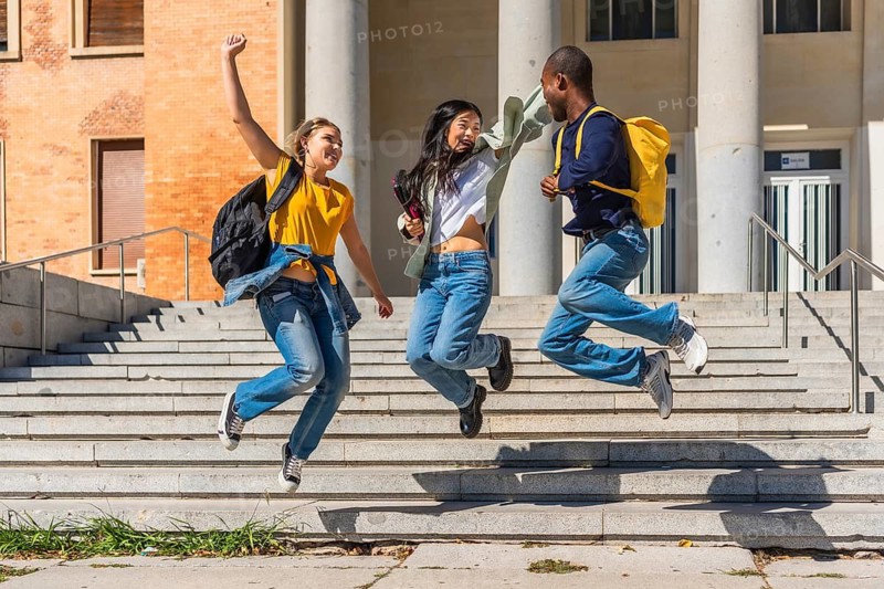 Three multi-ethnic cheerful university students jumping celebrating at the campus