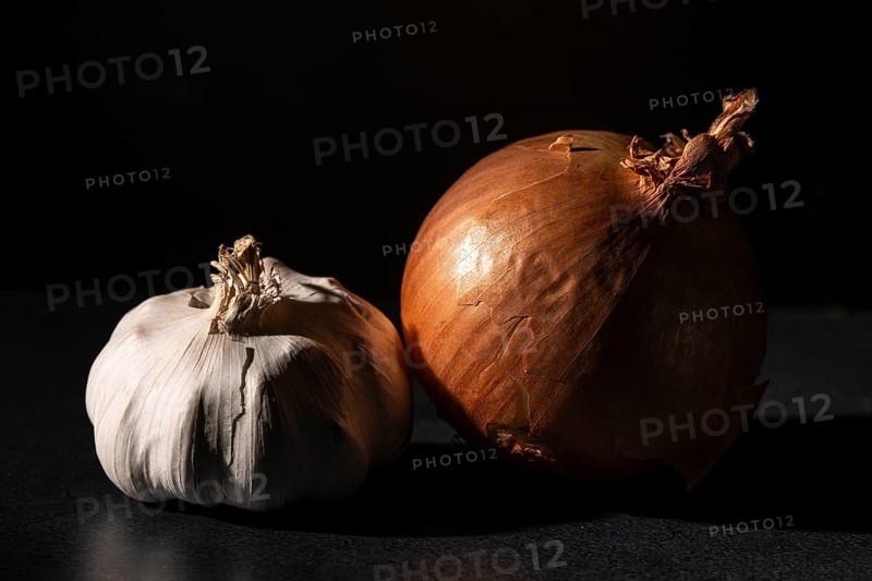 Garlic and an onion side by side, dramatically illuminated on a dark background