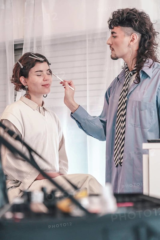 Professional makeup artist applying makeup on a model in a bright studio, enhancing her natural beauty with precision and skill for an upcoming photoshoot