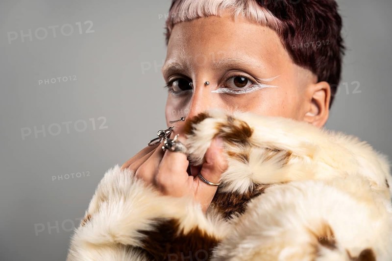 Close-up of a woman with striking makeup, bold rings, and a fur jacket. The expressive eyes and artistic makeup emphasize individuality and creativity in fashion