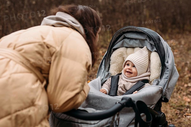 Mother and baby enjoy a delightful autumn walk in the park. The child, warmly dressed in a cozy outfit, smiles happily from the stroller as they bond outdoors