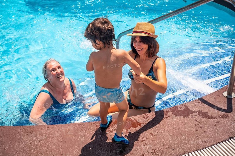 Mother and grandmother having fun with grandson in swimming pool on summer vacation, enjoying the water