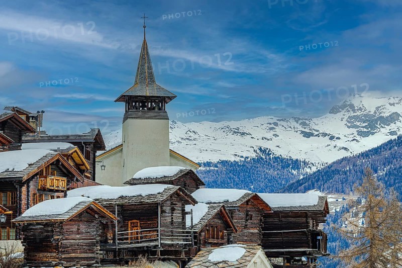 Old wooden houses with snow-covered roofs and the Saint Theodule church in the historic village centre, Grimentz, Val d'Anniviers, Valais Alps, Canton Valais, Switzerland