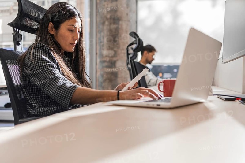 Two coworkers engaged in teamwork at a modern office The woman works on a laptop, indicating productivity and focus Sunlight filters through the window, creating a warm atmosphere